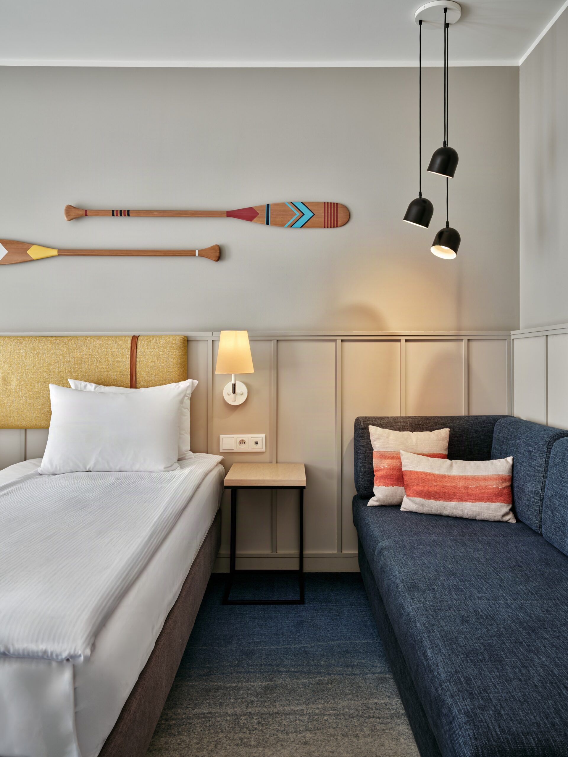Hotel room with two decorative wooden oars mounted on the wall above the bed, cream headboard, and a dark blue sofa with striped cushions.