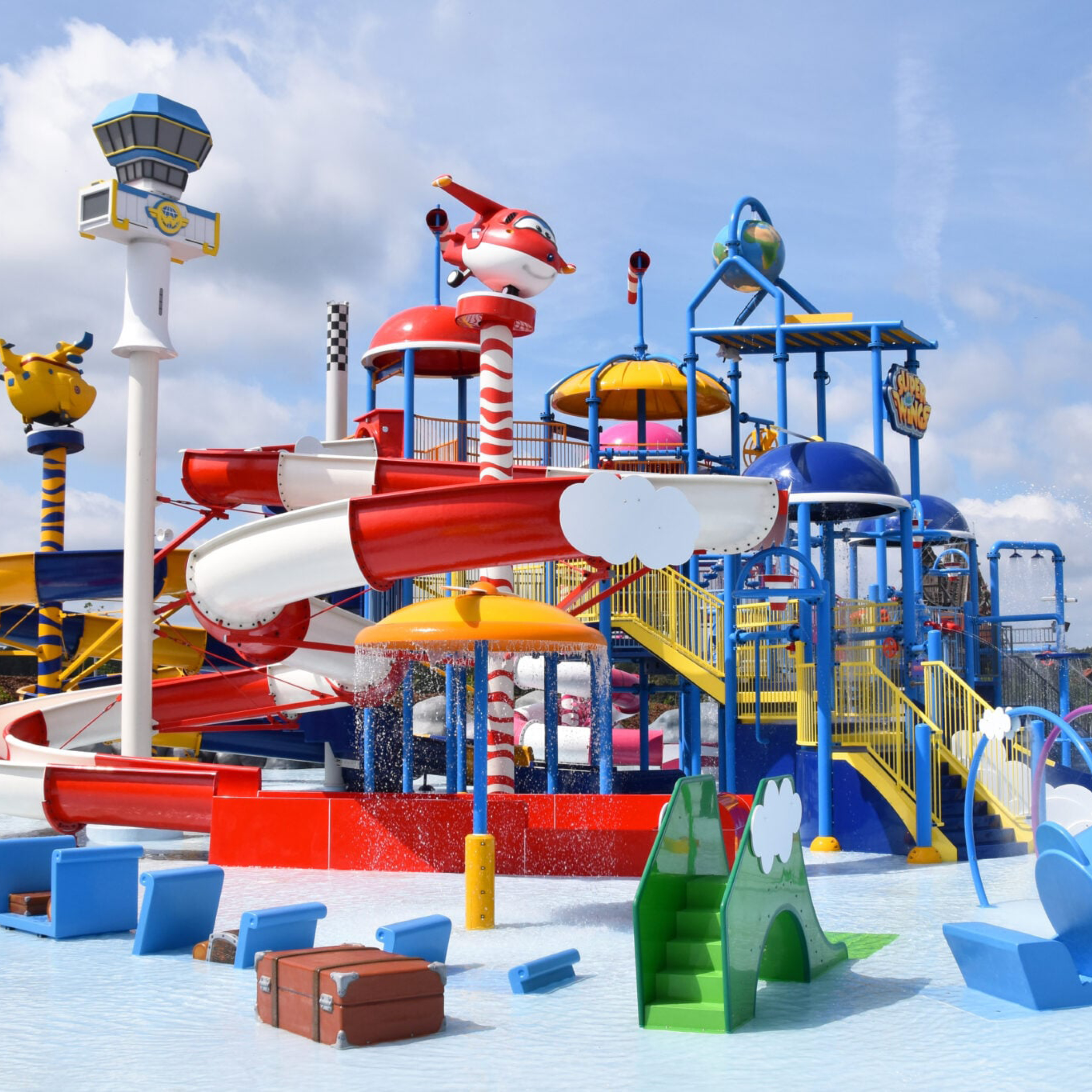 Colorful children's water park with bright red, blue, and yellow slides and playful animal figures against a blue sky.