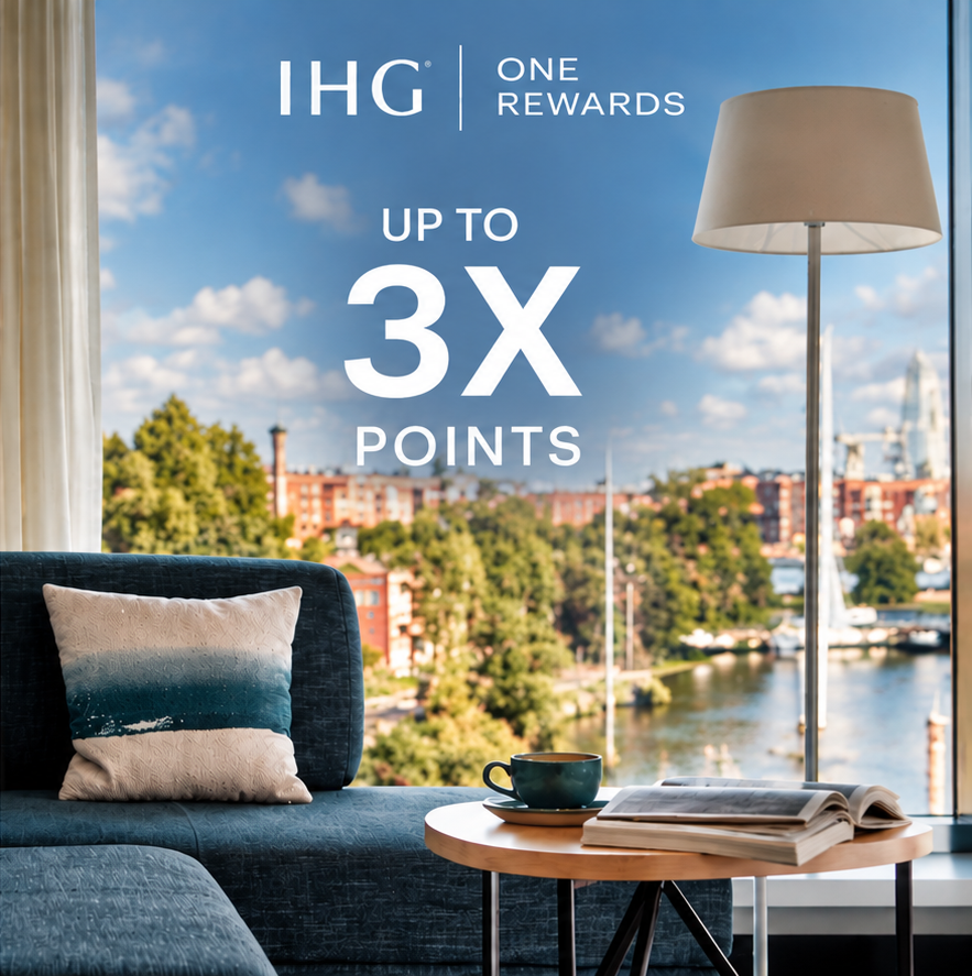 Interior living area with a blue couch by a large window showing a harbor; promotional text reads 'IHG One Rewards, Up to 3x Points'.
